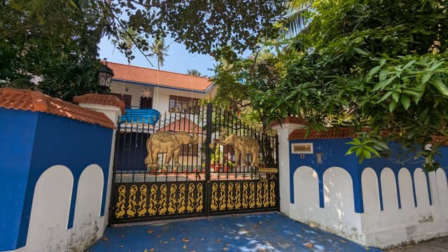 A gated entrance with blue and white walls leading to a house surrounded by greenery