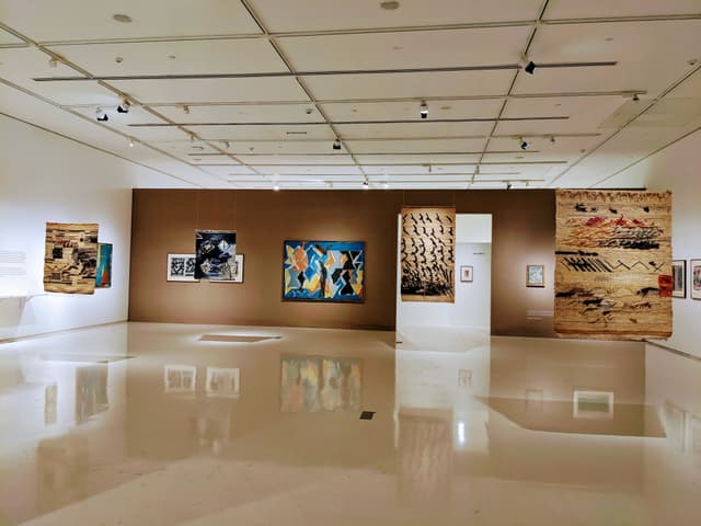 A modern art gallery with various paintings displayed on a brown feature wall and a reflective polished floor