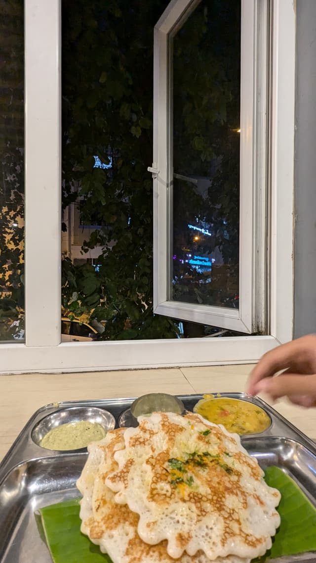 Stack of dosas on a metal tray next to an open window with a night view outside