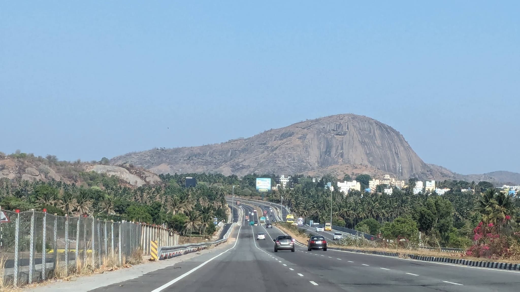 Multi-lane highway with cars and trucks curving toward a prominent rocky hill with sparse vegetation