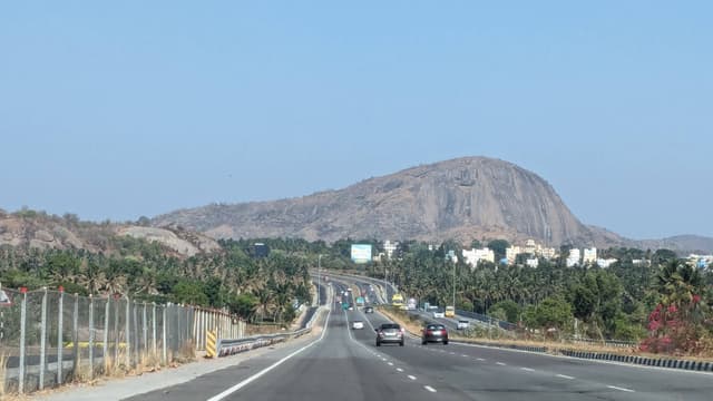 Multi-lane highway with cars and trucks curving toward a prominent rocky hill with sparse vegetation