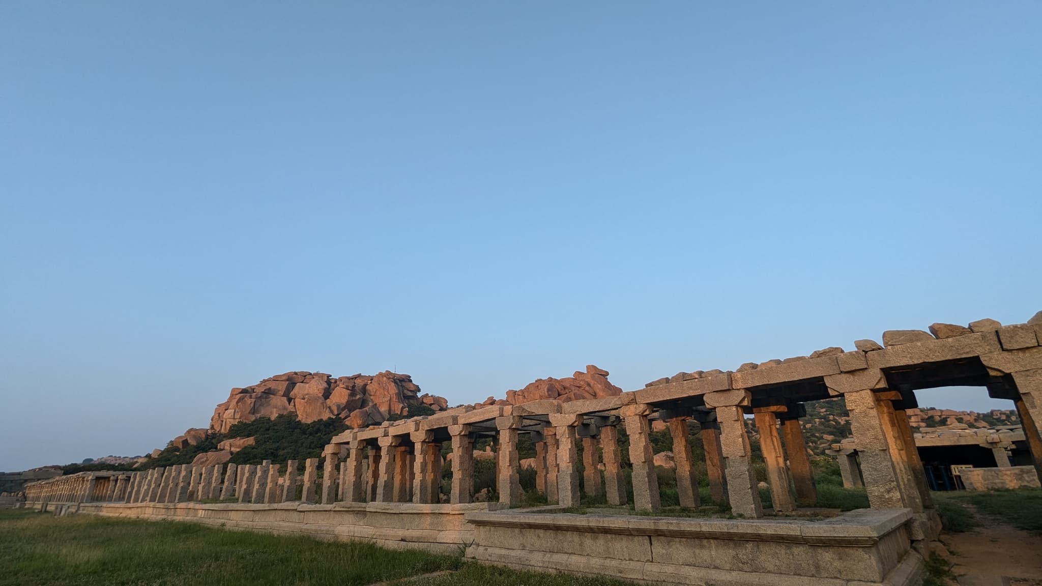 Ancient stone arches lead towards rocky hills under a clear blue sky