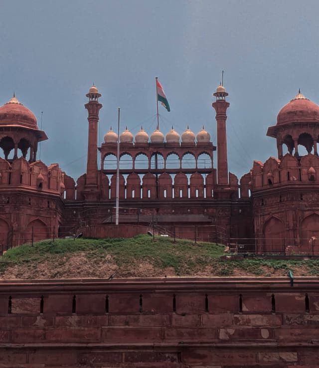 Historic red sandstone fort with Indian flag flying atop, featuring arched windows and domed structures against a clear sky