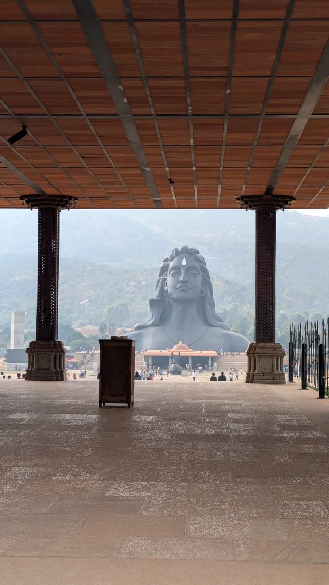 View from a covered pavilion toward the Adiyogi Shiva statue at the Isha Yoga Center, with mountains in the distance