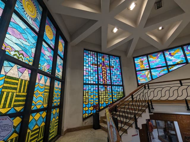 A stairwell featuring colorful stained glass windows with geometric and abstract designs, illuminated from behind, under a ceiling with a star-shaped pattern and recessed lighting
