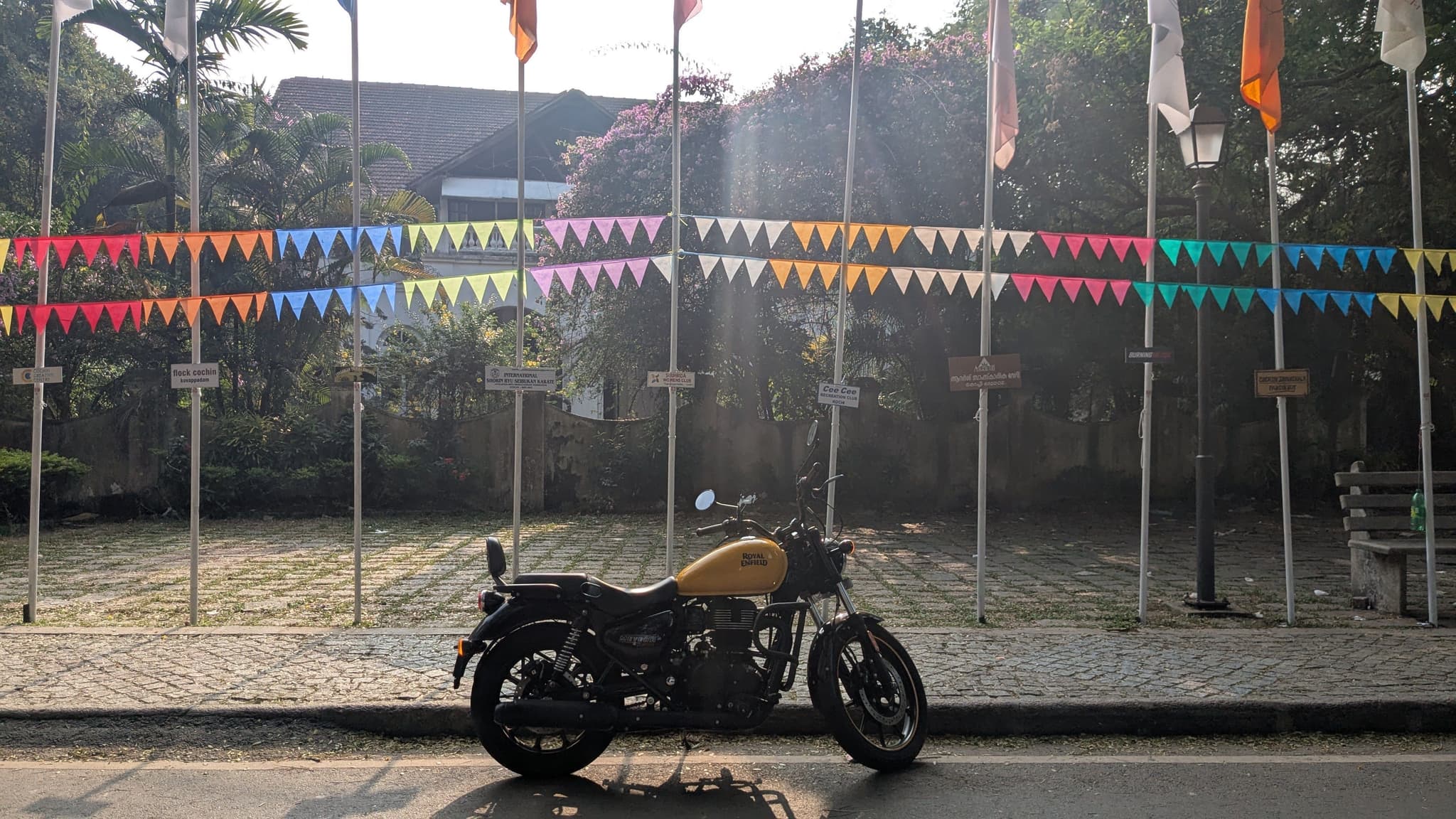 A parked motorcycle in front of a roadside fence decorated with colorful pennant flags and Indian tricolor banners