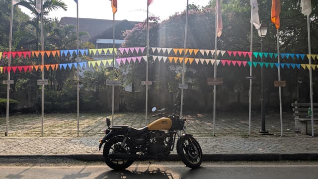 A parked motorcycle in front of a roadside fence decorated with colorful pennant flags and Indian tricolor banners