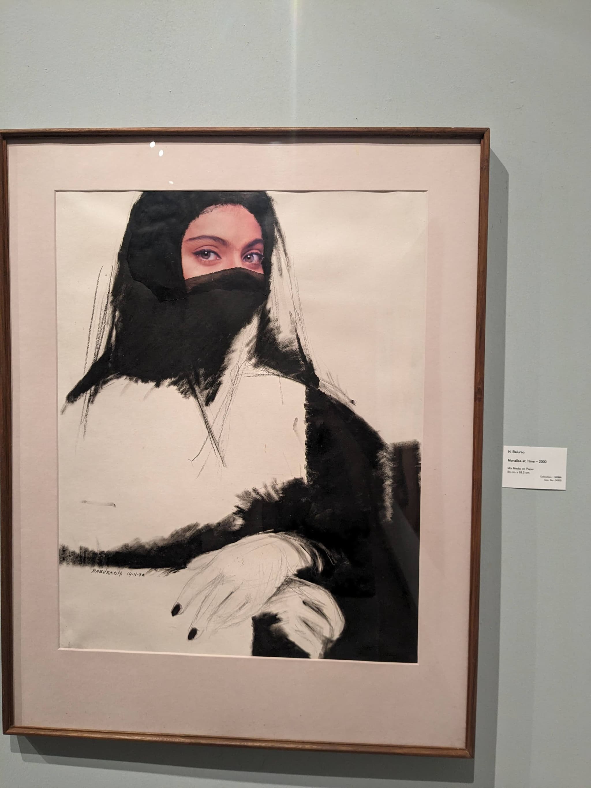 A framed artwork depicting a figure with a veiled face and crossed arms, featuring monochromatic colors with a touch of pink highlighting the eyes