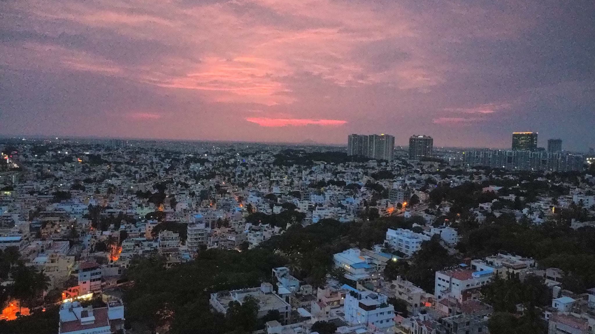 A wide cityscape at dusk with dense low-rise buildings and a pink sunset on the horizon