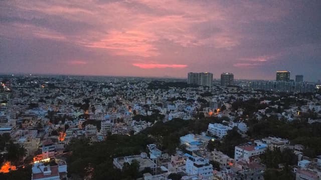 A wide cityscape at dusk with dense low-rise buildings and a pink sunset on the horizon