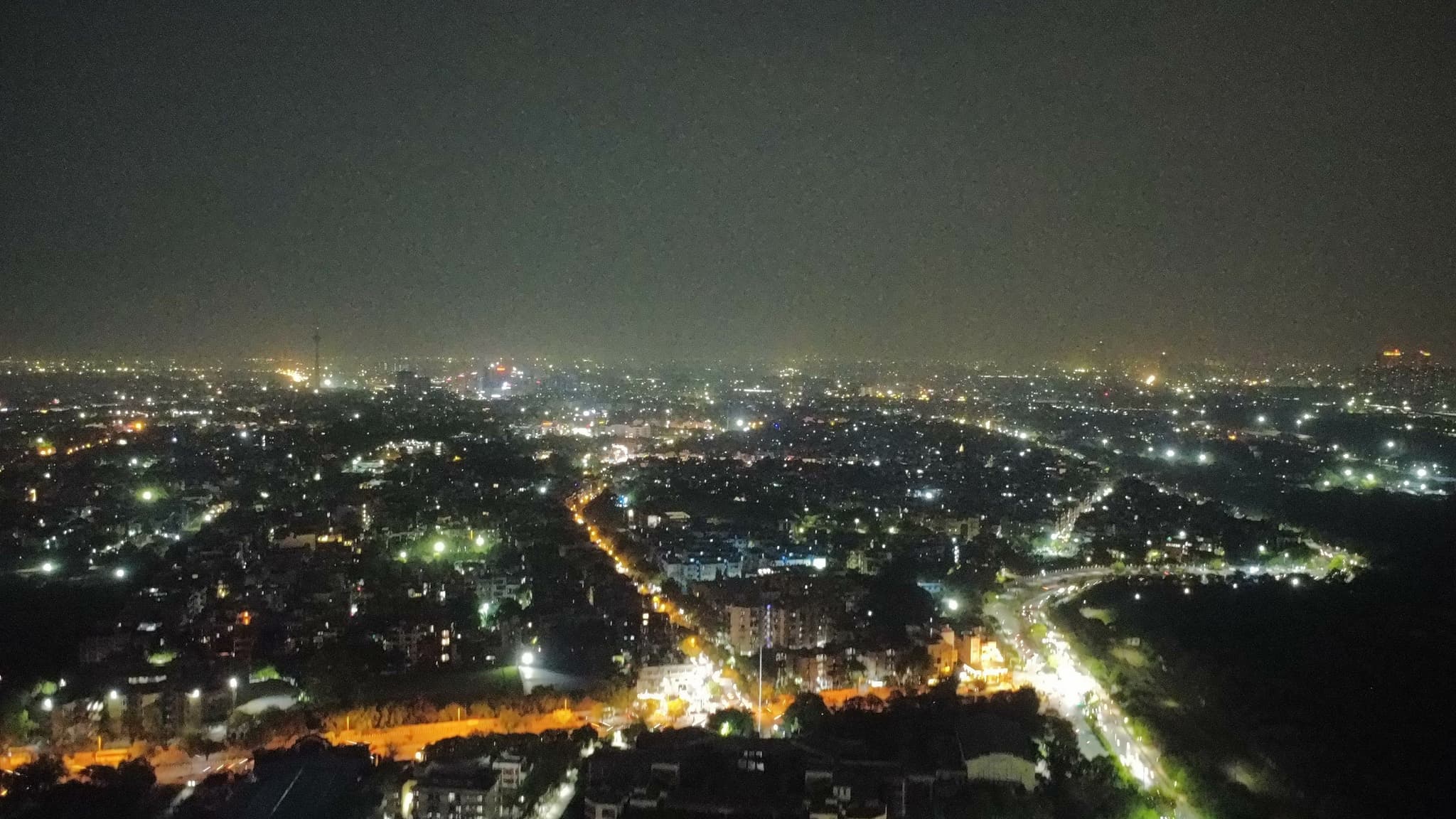 Aerial view of a city at night with dense clusters of lights and illuminated roads stretching into the distance